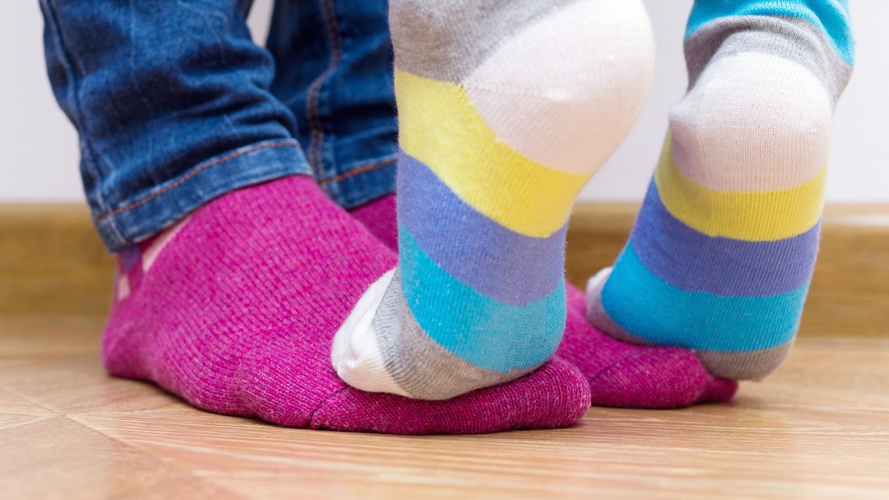 Ein Kind in Socken steht auf den Füßen der Mutter