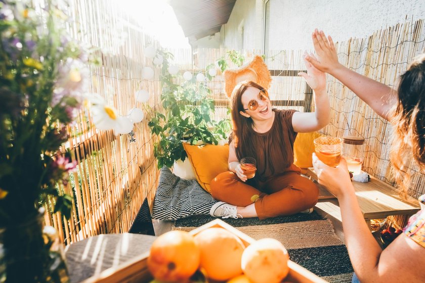 Joyful young woman clinks glasses with delicious cocktails with friend spending time together on decorated terrace on summer day close view.