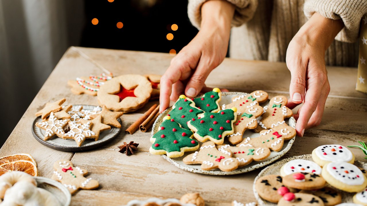 Woman hands arranging sweets on Christmas table. Close-up of female placing homemade gingerbread cookies and sweets on wooden table for Christmas celebration.