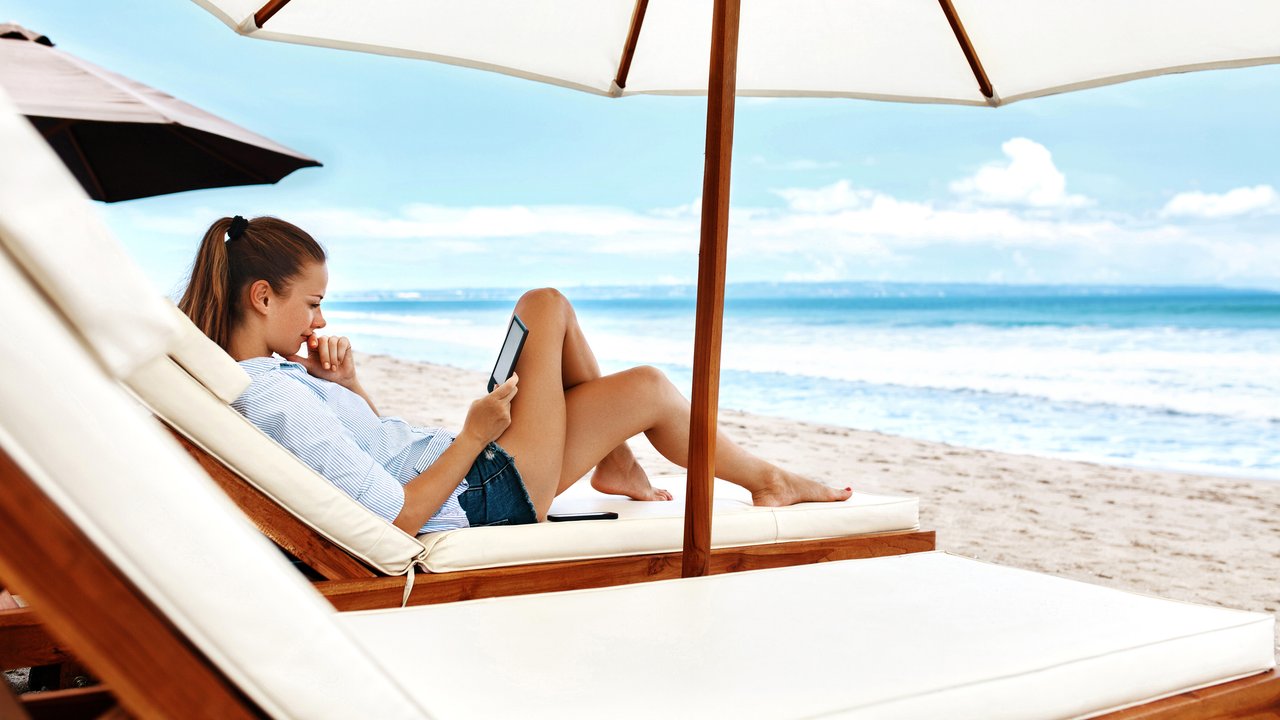 Summer Relaxation. Beautiful Woman Reading E-Book, Relaxing On Sun Lounger, Deck Chair Under Umbrella, Tent On Beach By Sea. Summertime. Holiday Vacations. Leisure, Recreation, Enjoyment Concept