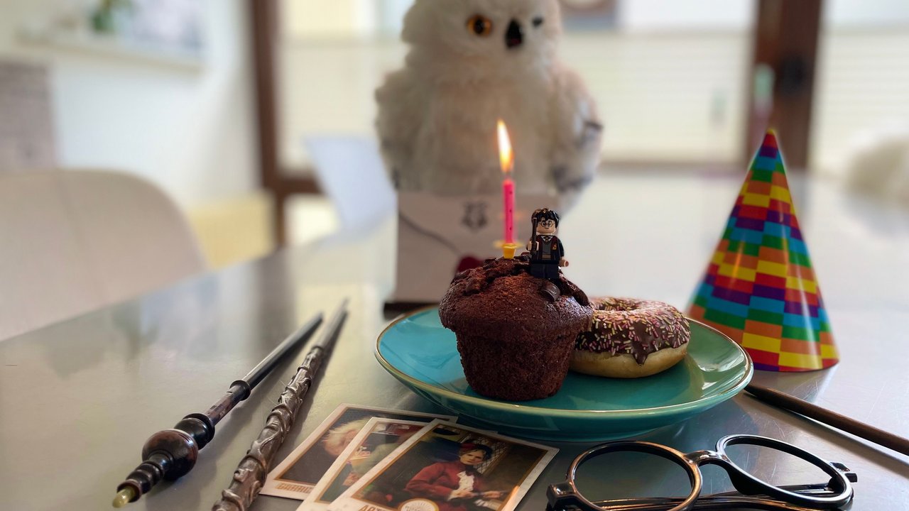 Harry Potter Geburtstag: Kleiner Kuchen mit Kerze und Harry Potter Figur steht auf Tisch mit Eule, Zauberstäben, Brille und Partyhütchen