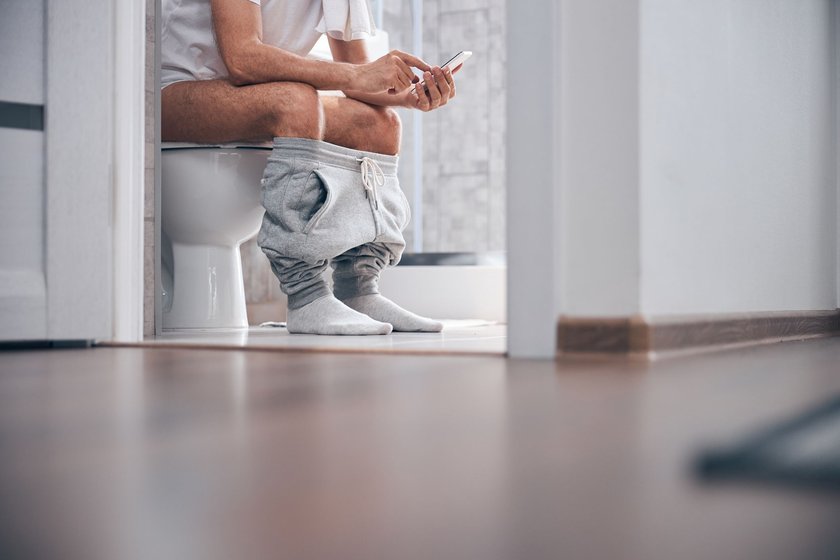 Mann sitzt mit dem Handy auf der Toilette