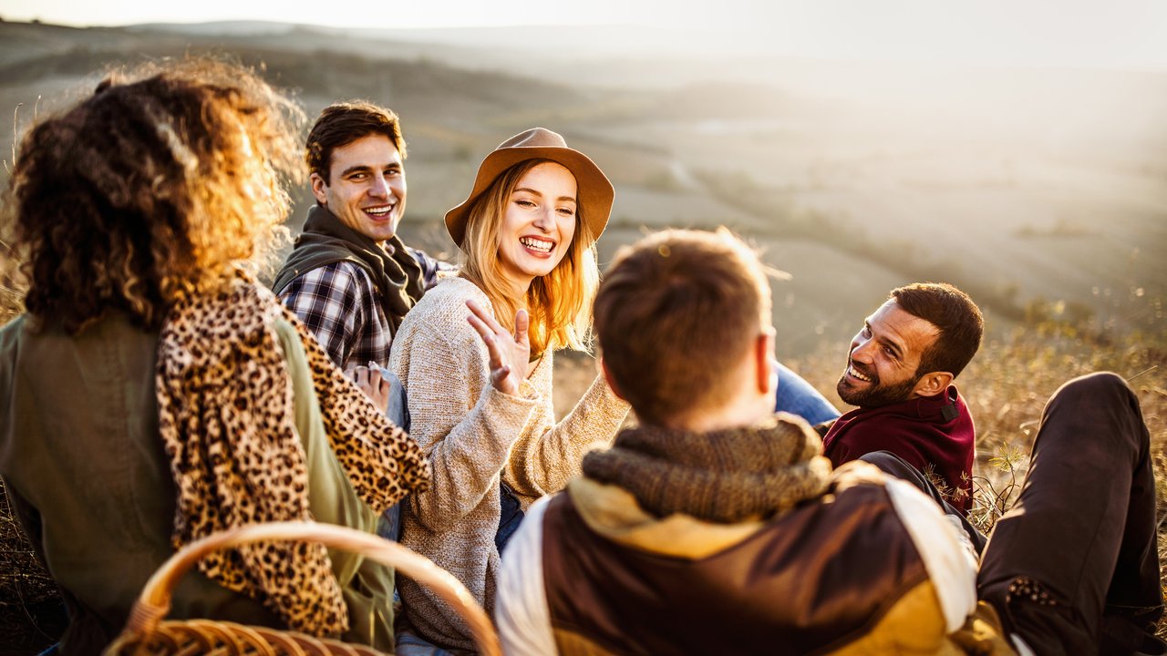 Young happy friends communicating while enjoying in picnic during autumn day.