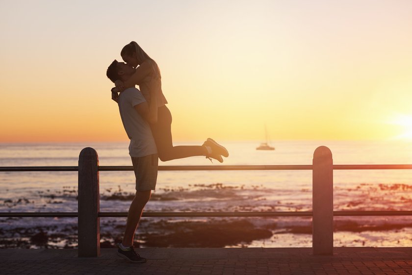 Young woman jumps on boyfriend and gives him a kiss at sunset, romantic passionate moment on date, golden sun flare