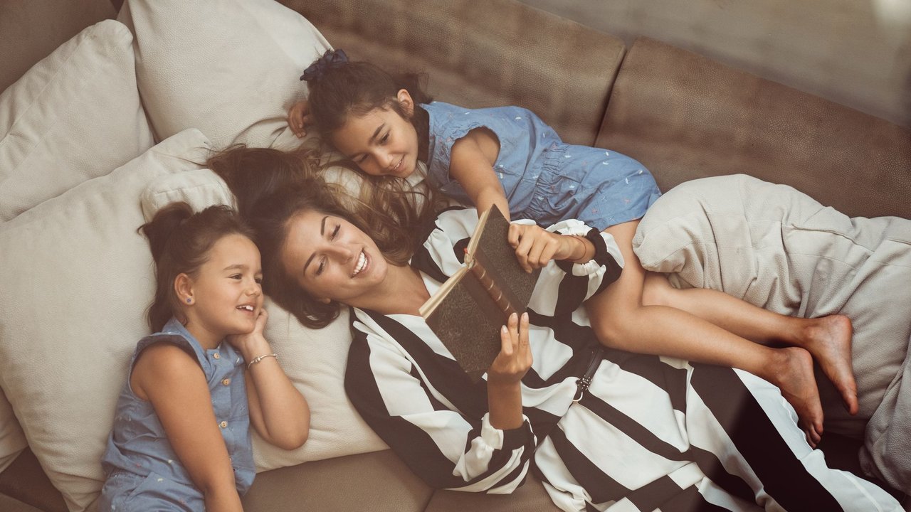 Relaxed woman with two daughters on the sofa reading a book