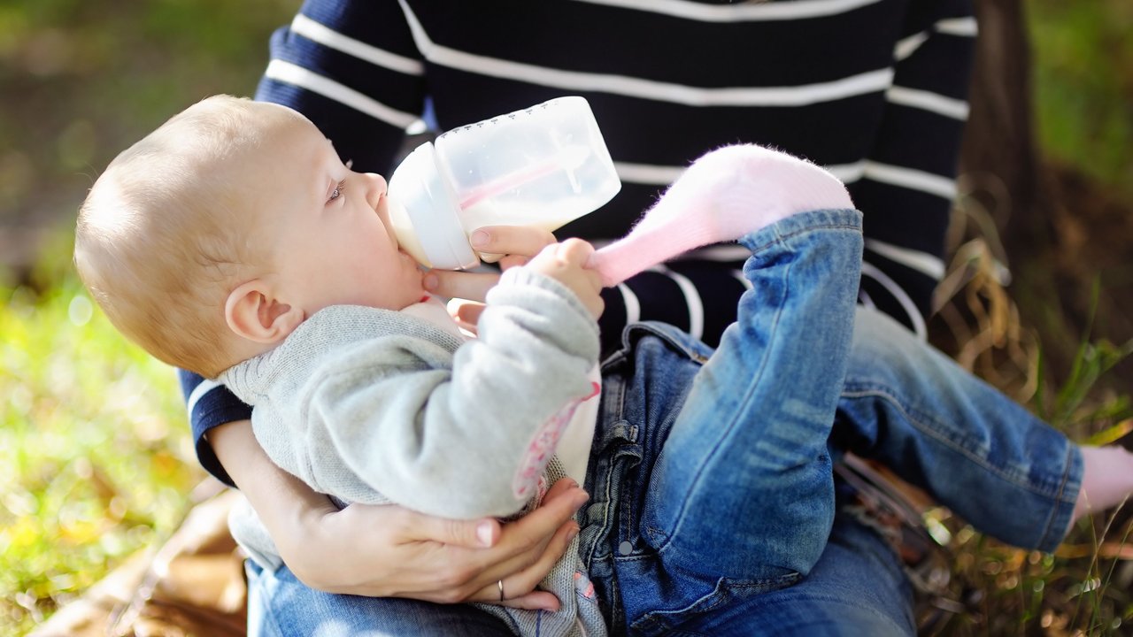 Baby wird im Park mit Flasche gefüttert