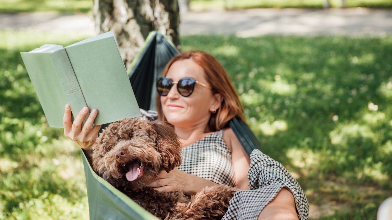 Frau mit Hund liegt in einer Hängematte und liest