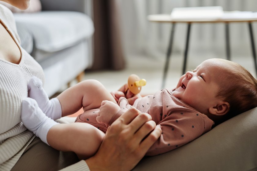 Side view of mother playing with laughing baby girl lying on her knees spending time at home