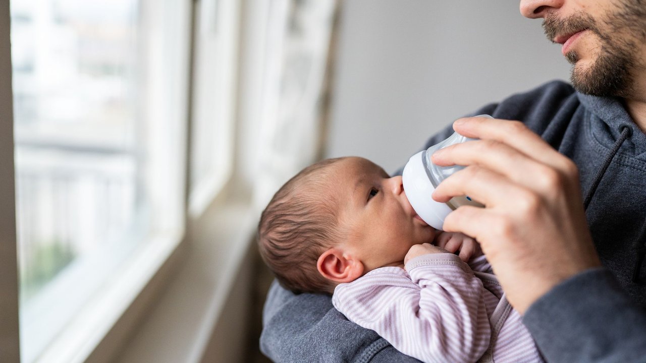 Mann füttert Baby mit Flasche am Fenster