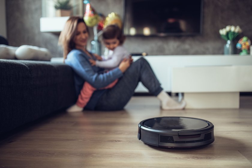 Robotic Vacuum Cleaner Cleaning Floor While Mother and Daughter Playing on the sofa