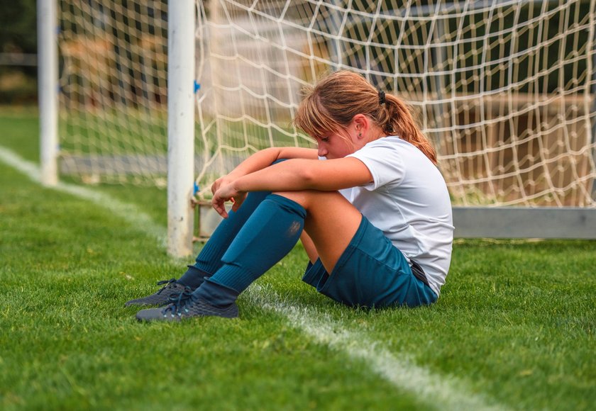 Kind sitzt enttäuscht auf dem Fußballplatz