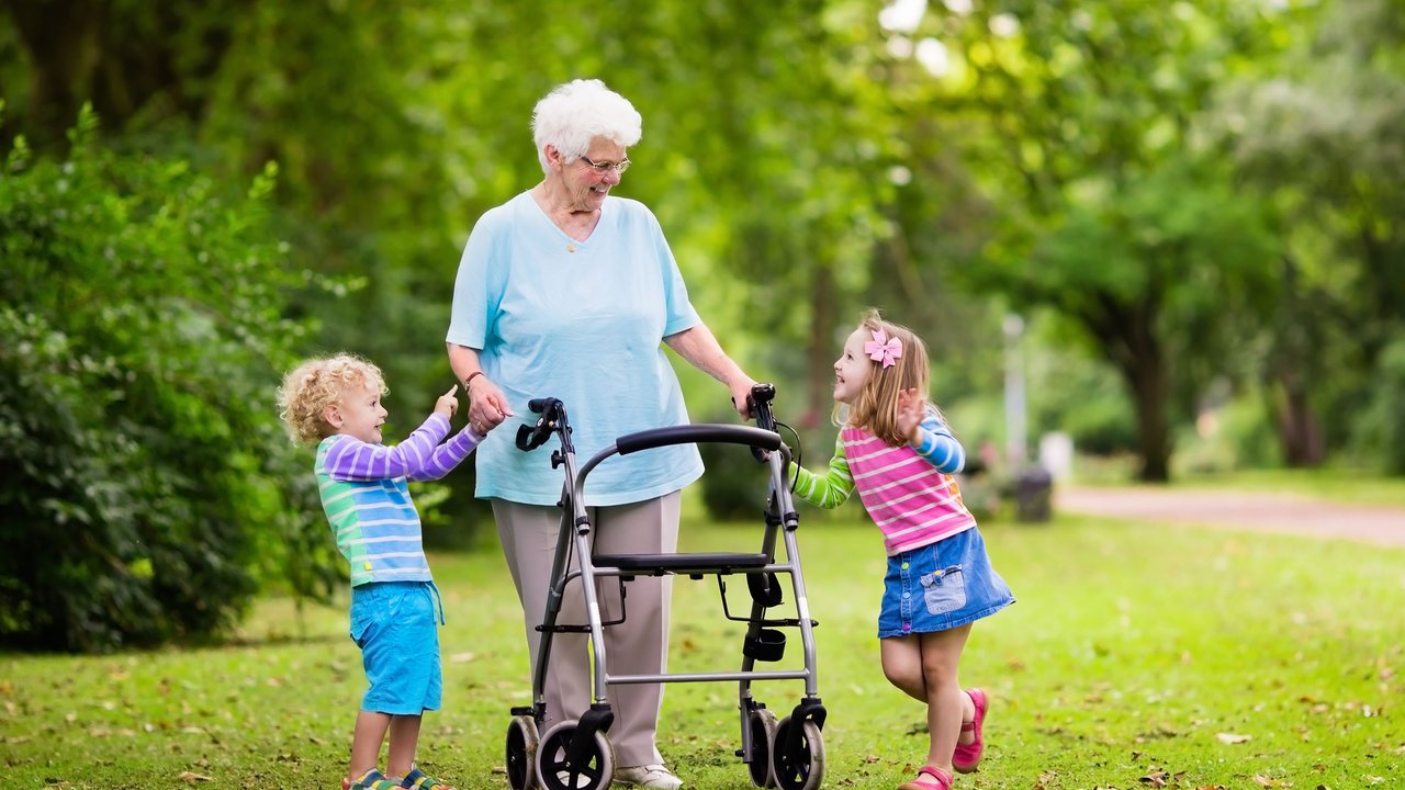 Oma ist mithilfe eines Rollators mit ihren Enkelkindern im Park unterwegs