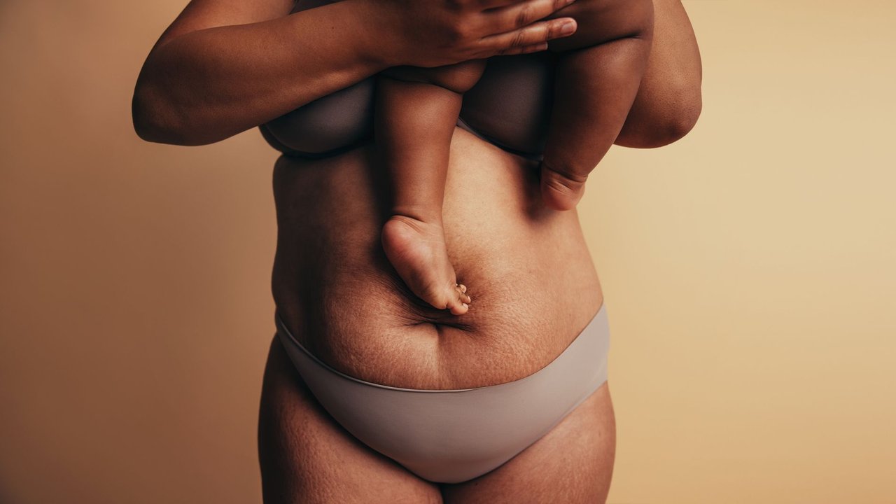Abnehmen nach der Schwangerschaft: Frau in Unterwäsche mit Baby auf dem Arm