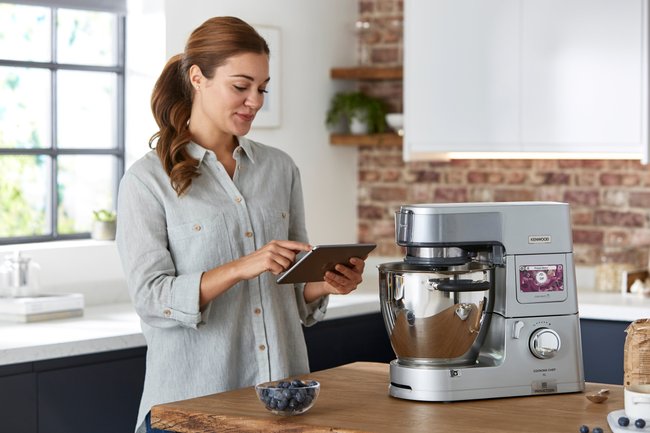 Eine Frau mit einem Tablet in der Hand, vor ihr steht die Kenwood Cooking Chef XL.