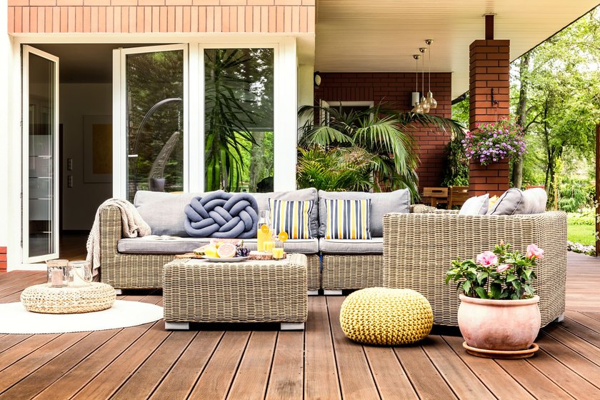 Beige garden furniture with striped pillows on wooden terrace with pink flowers and poufs