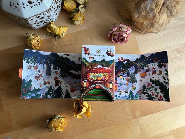 Sonnentor Tee-Adventskalender mit Keksen und Blumen im Hintergrund