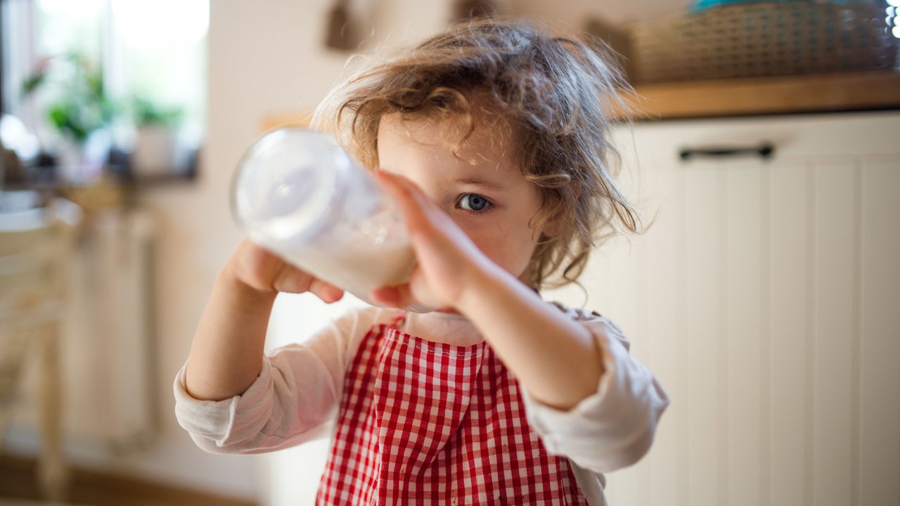 Kleines Mädchen sitzt in Küche und trinkt Milch aus einer Flasche