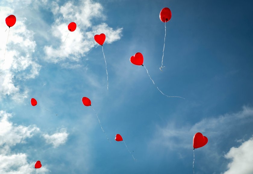 Valentinstag-Sprüche: Rote Luftballons in Herzform fliegen in blauen Himmel mit weißen Wölkchen