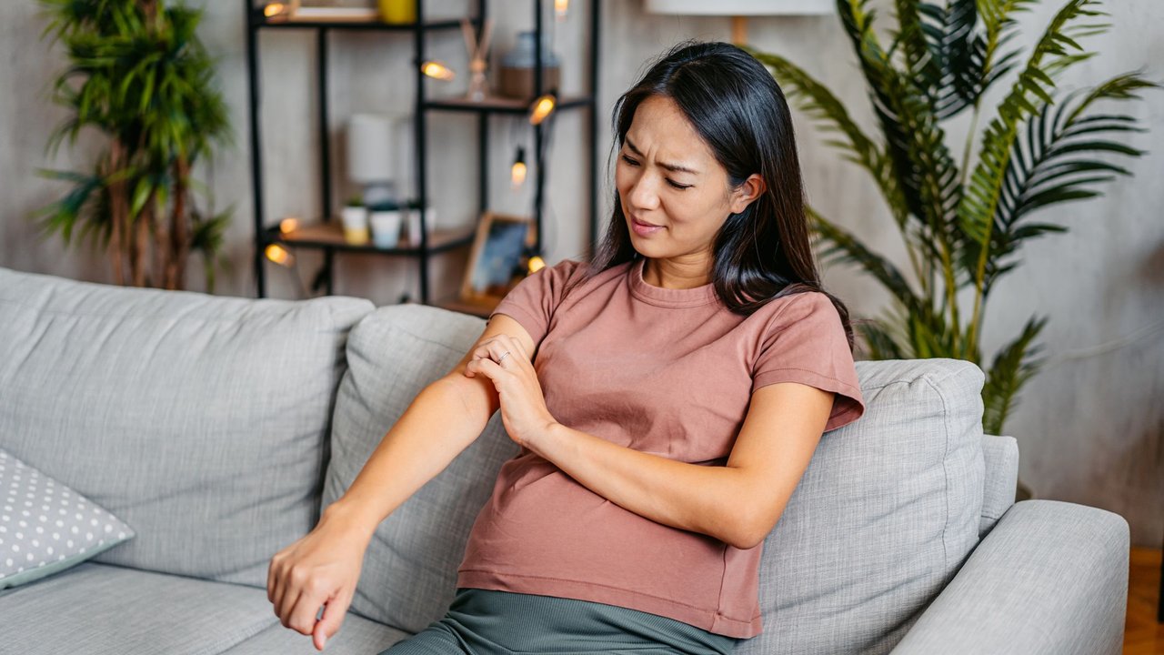 Schwanger Frau sitzt auf Sofa und kratzt sich am Arm