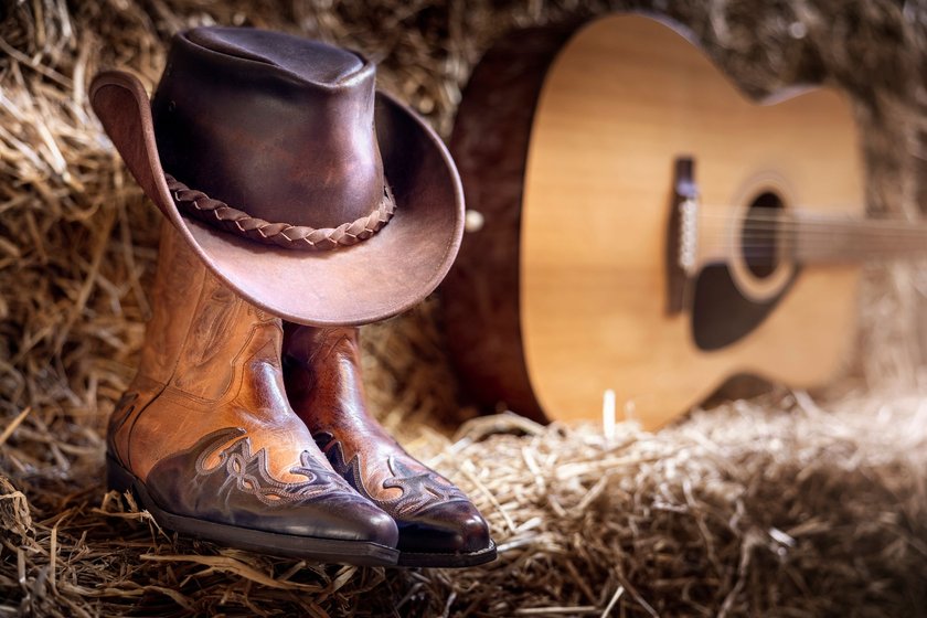 Cowboy-Stiefel und -Hut mit Gitarre im Stroh