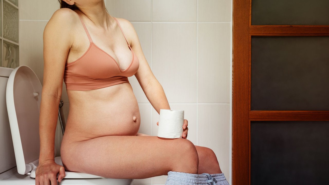 Schwangere Frau sitzt nach Einlauf vor der Geburt auf der Toilette.