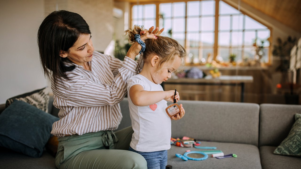 Haargummitrick: Mother styling her little daughter's hair while playing with makeup at home