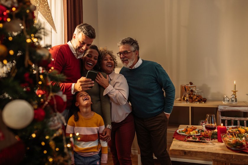 Happy family is standing next to the Christmas tree, checking out a selfie they took after Christmas family dinner and smiling