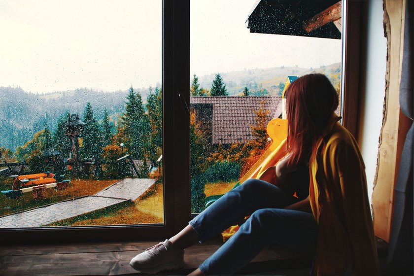 Frau sitzt am Fenster und sieht dem Regen zu