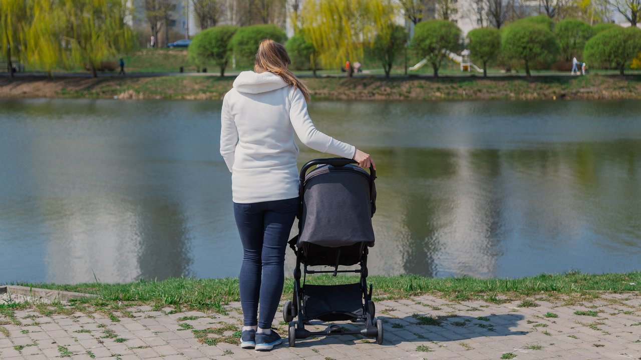 Young mother with a baby in a stroller by the lake in summer
