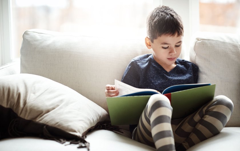 Shot of an adorable little boy reading a book while relaxing on the sofa at home