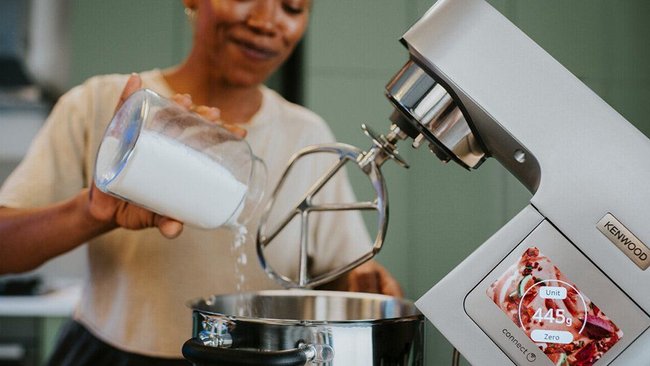 Eine Frau, die Mehl in den Behälter einer Küchenmaschine kippt.