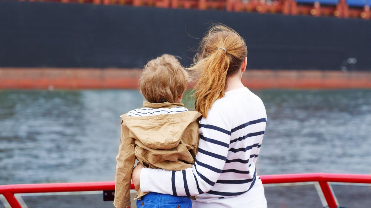 Frau mit Kind am Hamburger Hafen guckt auf ein Containerschiff