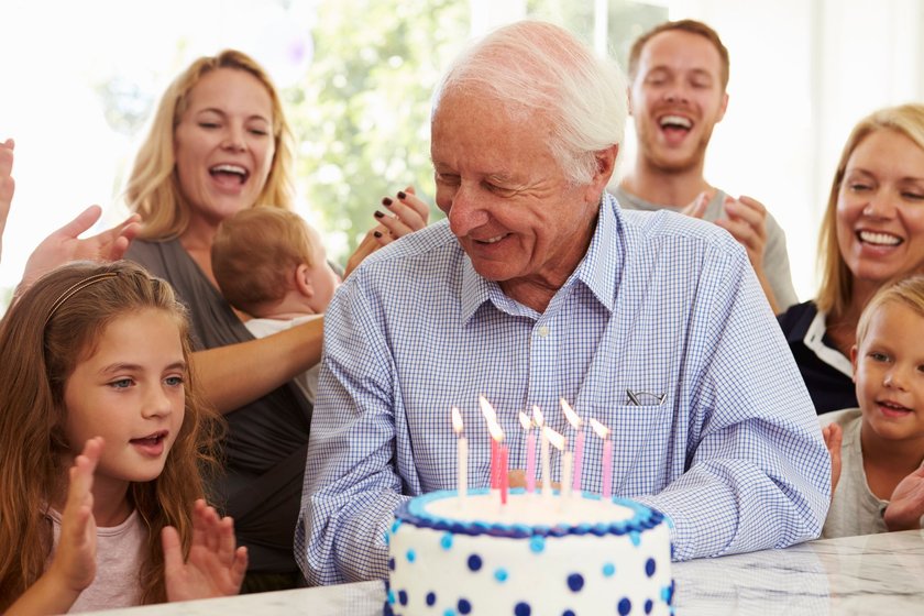 Glückwünsche zum 80. Geburtstag: Älterer Mann mit Geburtstagstorte lacht im Kreise seiner Familie