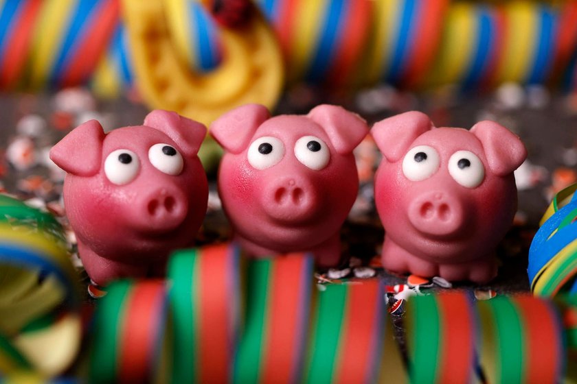 Drei kleine Schweinchen aus Marzipan sitzen zwischen Luftschlangen und Konfetti auf einem Tisch.