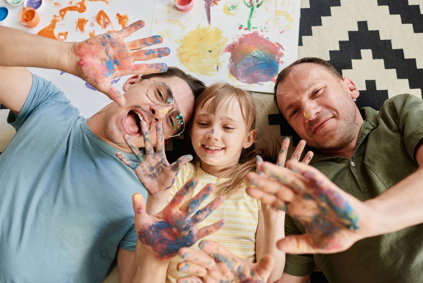 High angle view of happy gay family lying on the floor with their daughter showing their painted hands and smiling they painting at home