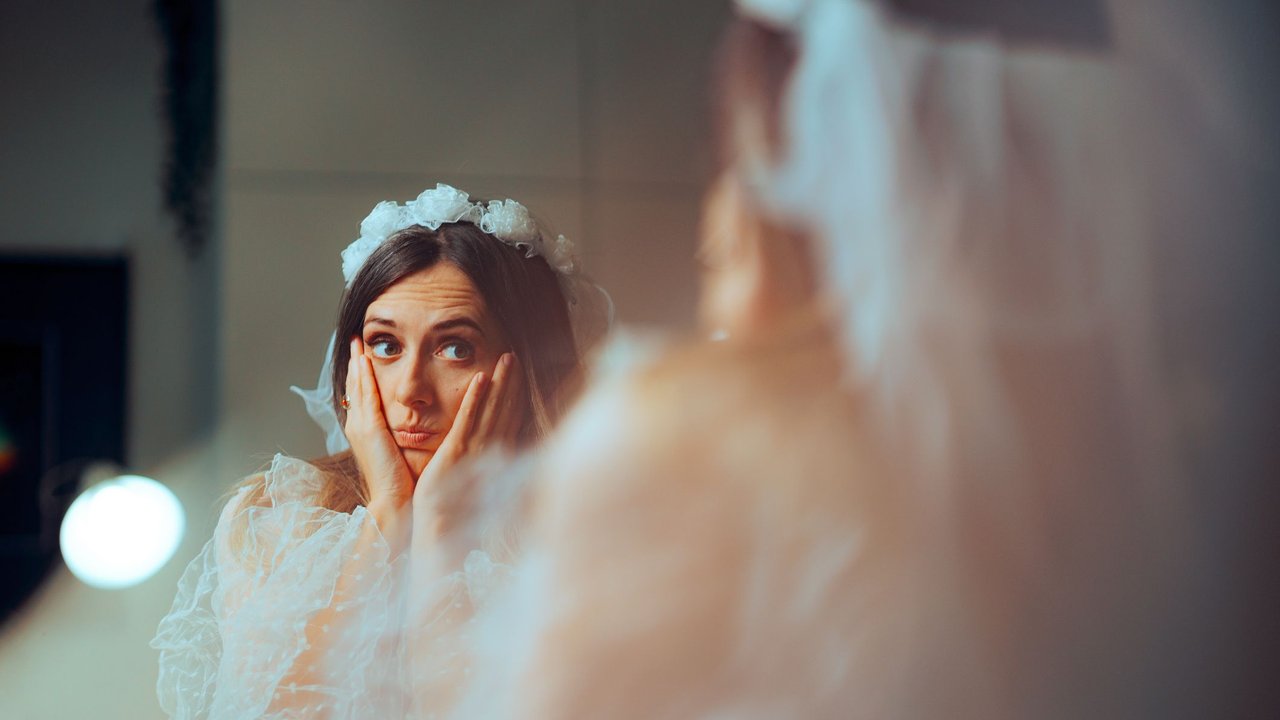 Unsichere Braut steht zweifelnd vor dem Spiegel am Tag der Hochzeit