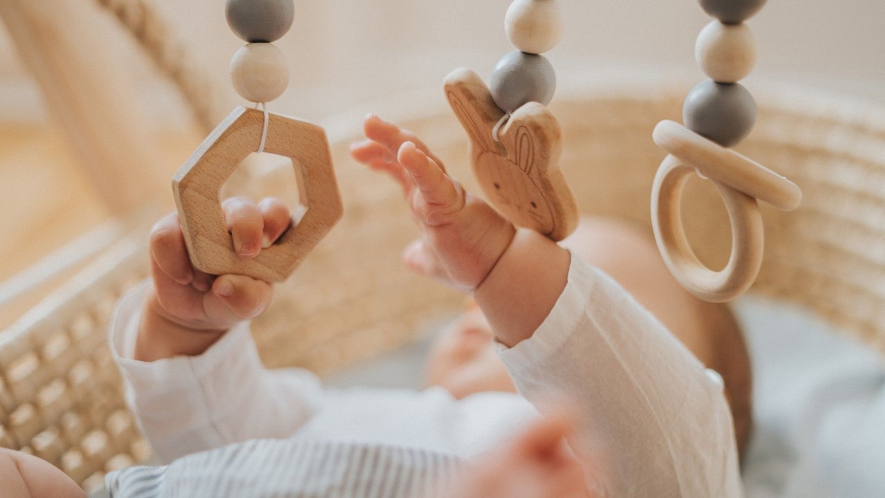 Frühkindliche Reflexe: Baby greift nach Holzspielzeug