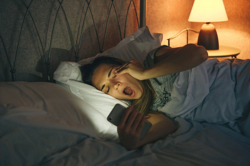 Frau liegt nachts wach mit Handy im Bett