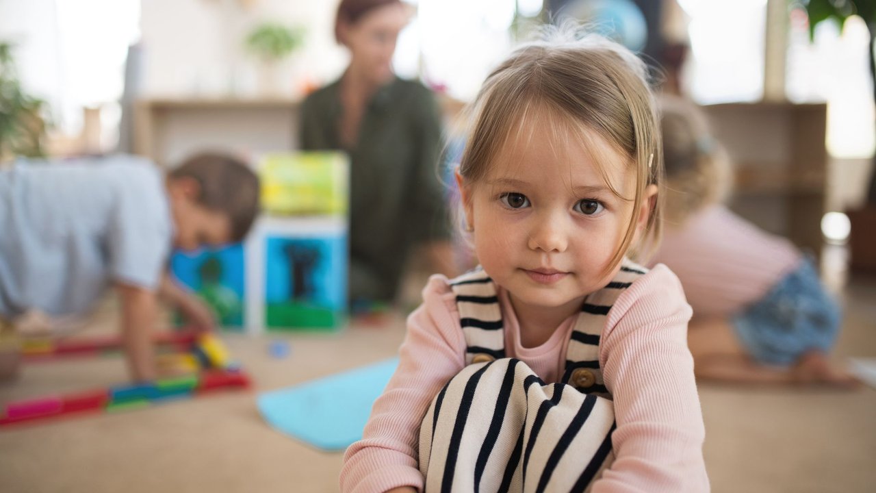 Ist der Kindergarten Pflicht: Mädchen sitzt in Kindergartenraum und schaut in die Kamera