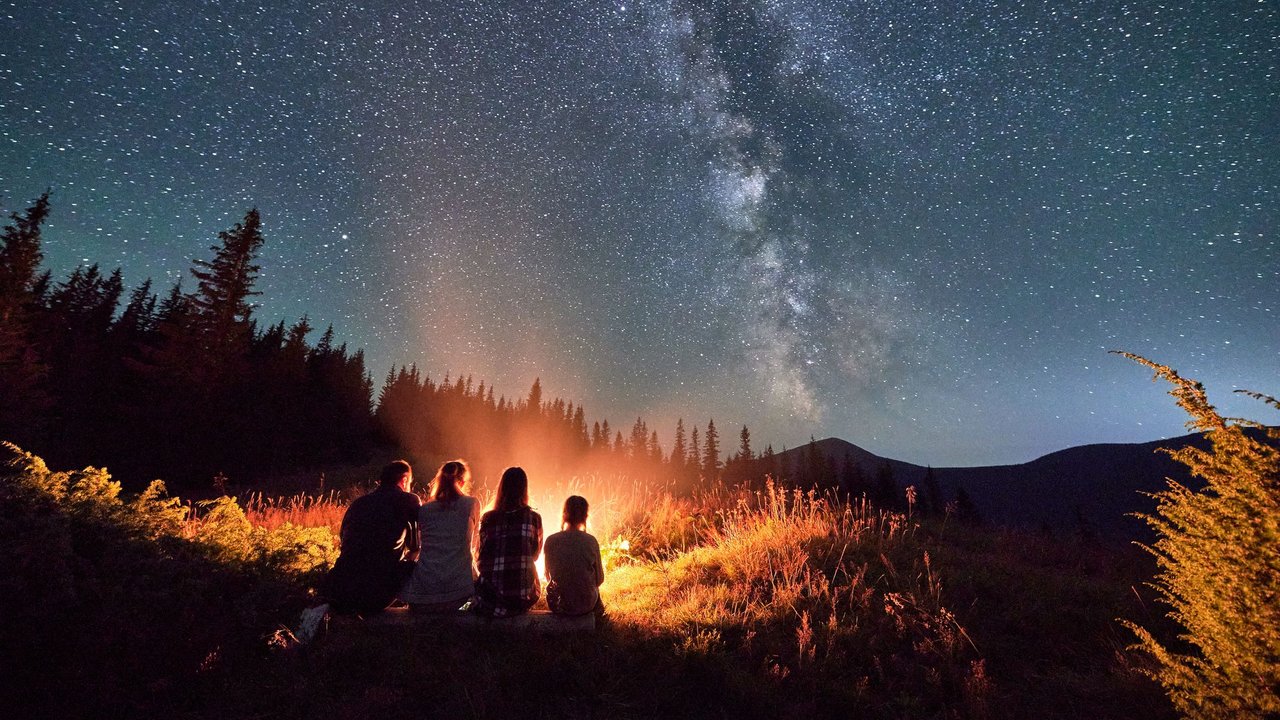 Familie sitzt vor einem Lagerfeuer unter dem Sternenhimmel