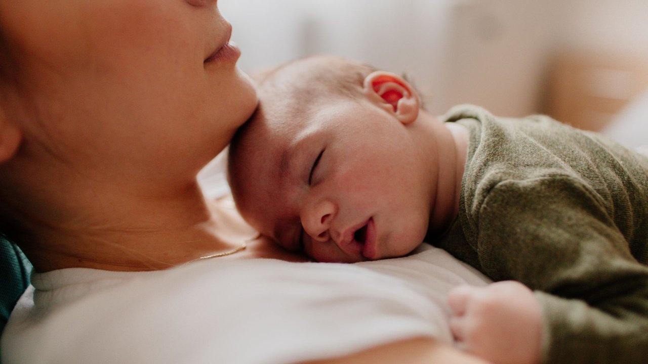 Photo of a young mother holding her newborn baby, while putting him to sleep