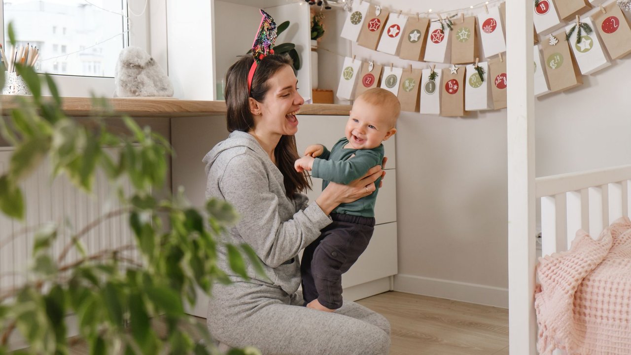 Mother with infant child having fun Christmas advent calendar tasks and gifts. Baby boy excited about festive surprise and play at home. Family celebration and preparation for New Year