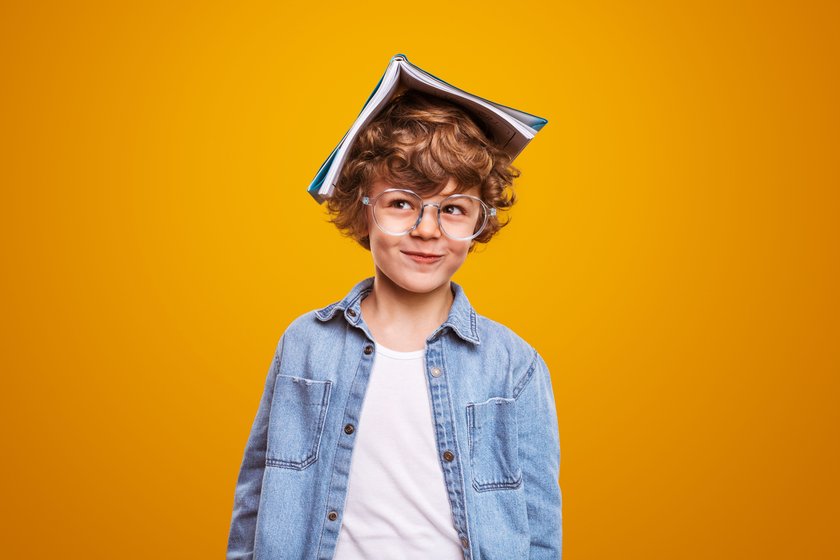 Neugieriger Schüler mit Lehrbuch auf dem Kopf