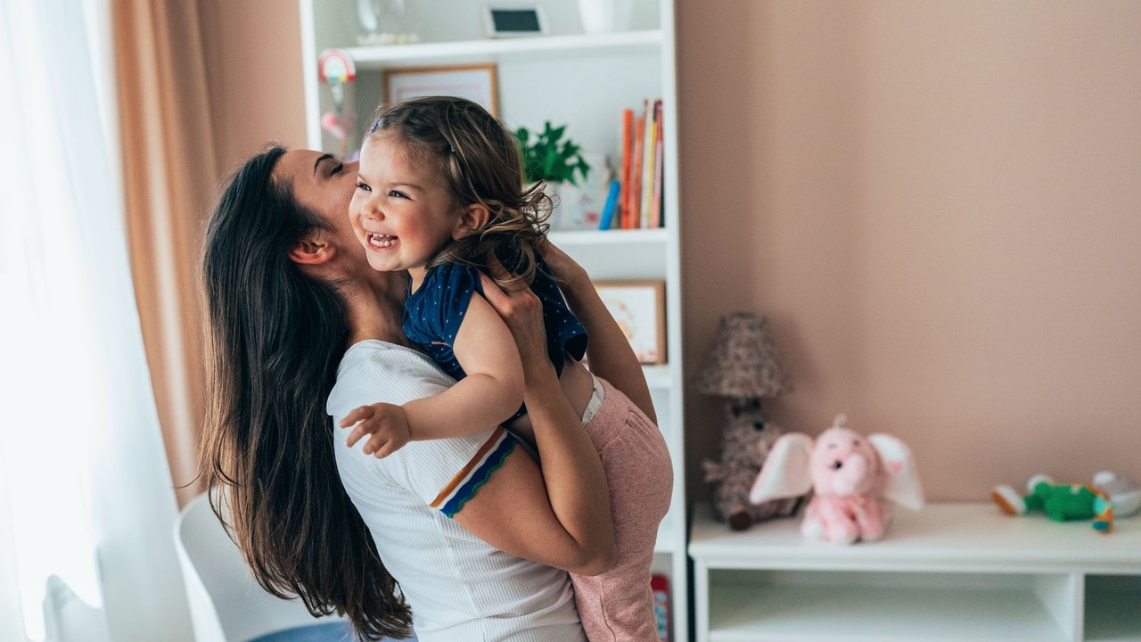 Montessori für Anfänger: Lachende Mama hält im Kinderzimmer lachendes Kind auf dem Arm.