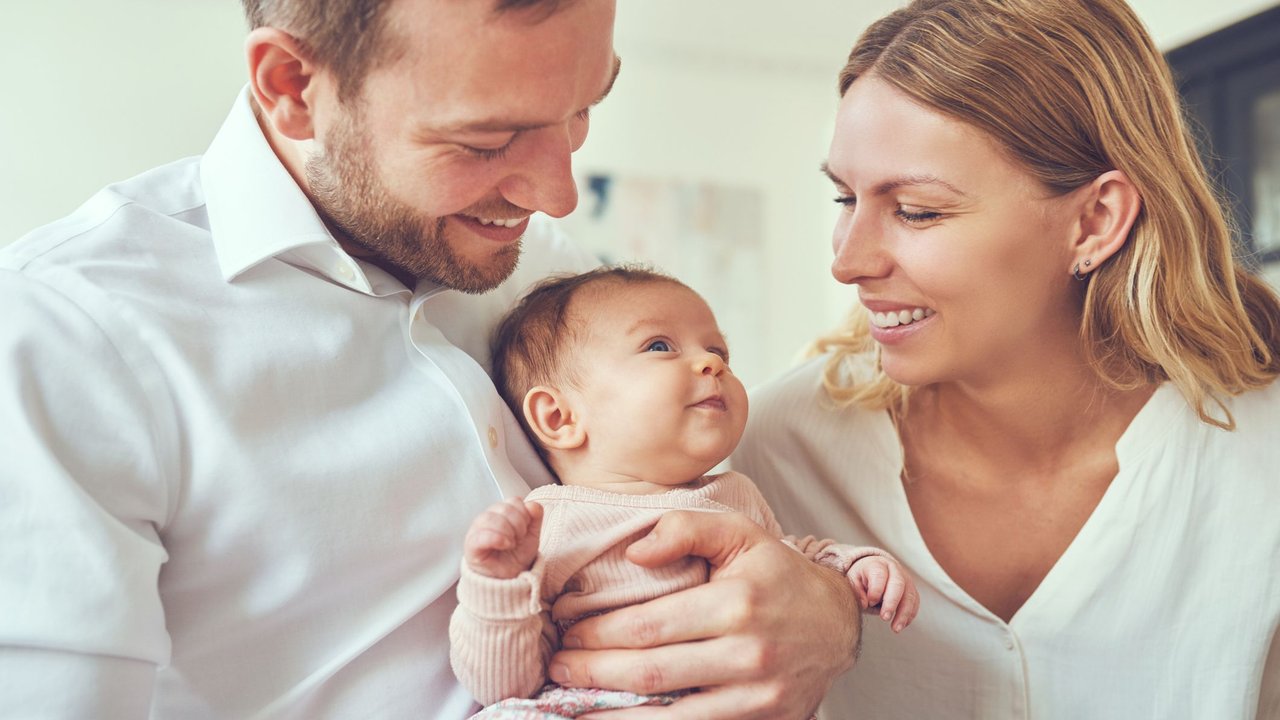 Text für die Dankeskarte nach der Geburt: Vater hält Baby, Mutter lächelt es an