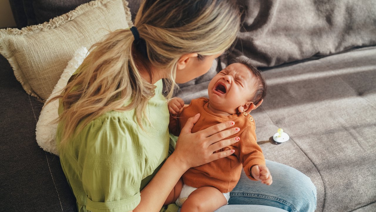 Baby mit Bauchweh weint im Arm seiner Mama