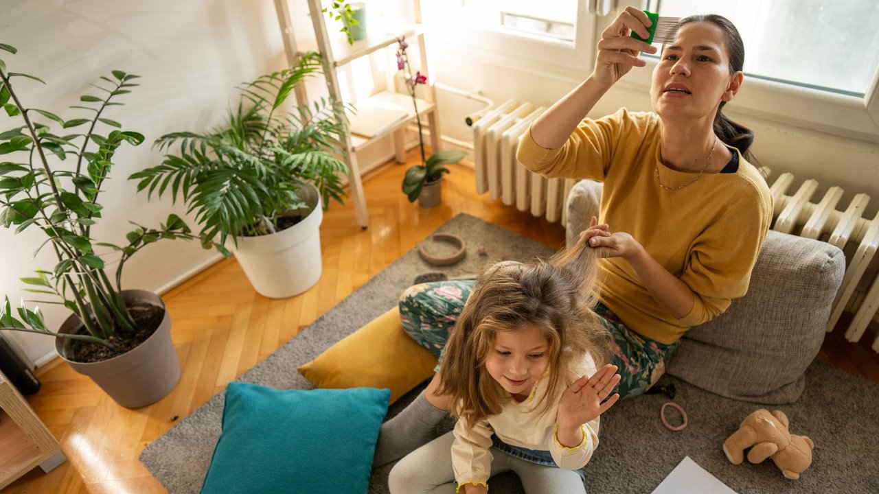 Frau mit Kind auf Sofa beim Auskämmen von Läusen