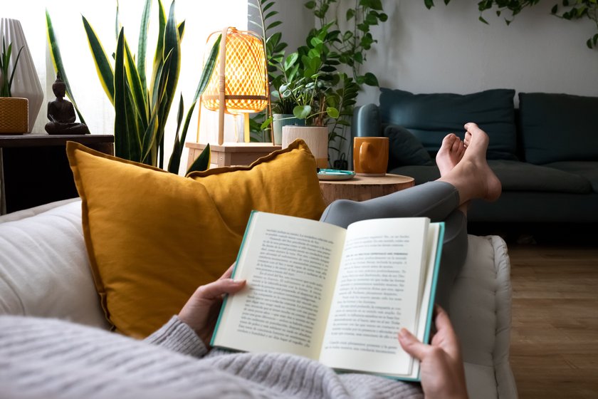 POV of young woman relaxing at home reading a book lying on sofa. Lifesyle concept.