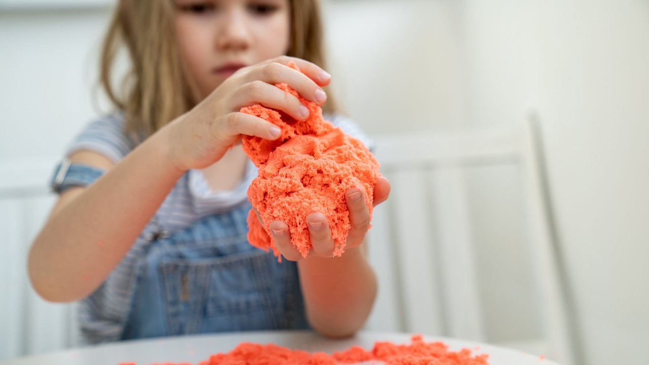 Kleines Mädchen spielt mit orangefarbenem kinetischen Sand