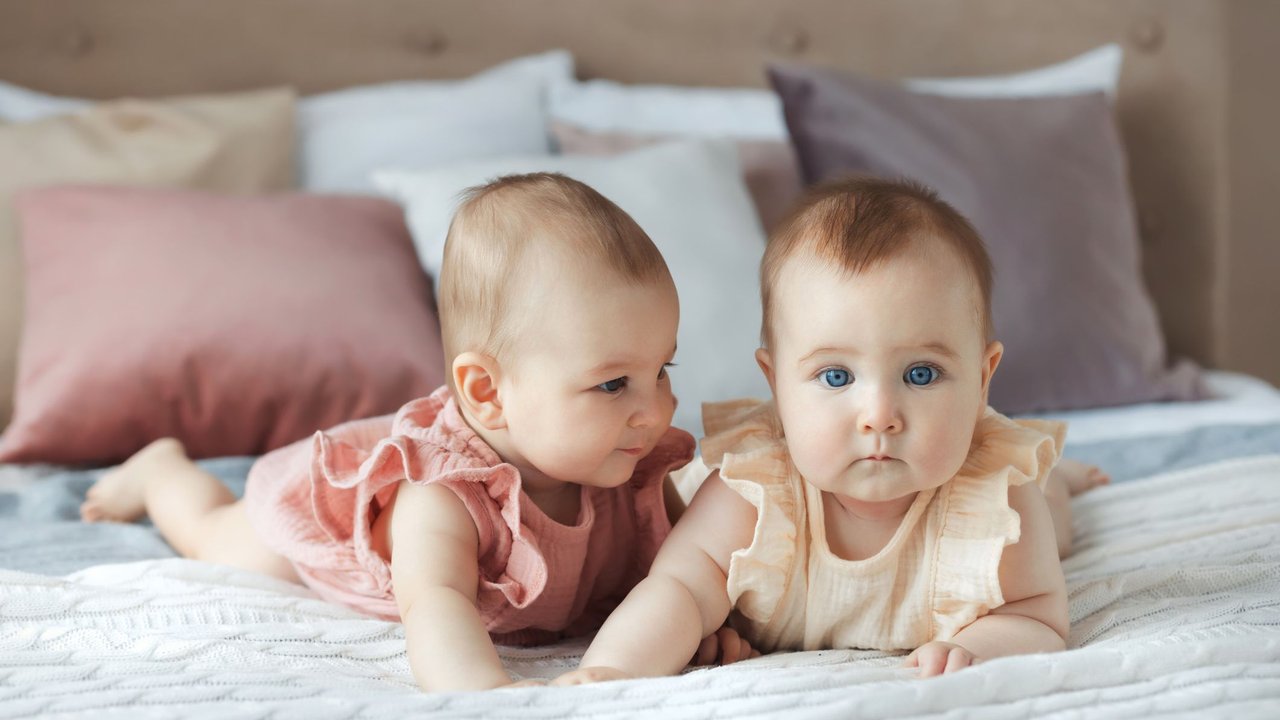 Zweieiige Zwillinge: Geschwister-Babys liegen auf einem Bett